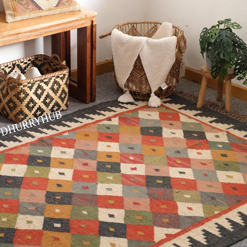 May include: A multicoloured geometric patterned rug with a black border and fringe. The rug is made of natural fibres and has a rustic, hand-woven look.