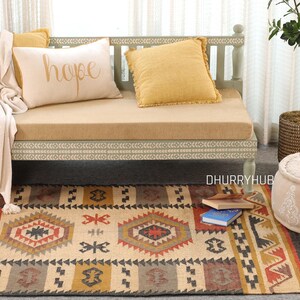 May include: A light green wooden daybed with a beige cushion and throw blanket. The daybed has a white and gray patterned trim. The daybed is decorated with three throw pillows, one with the word "hope" embroidered on it. A beige and brown patterned rug is in front of the daybed.