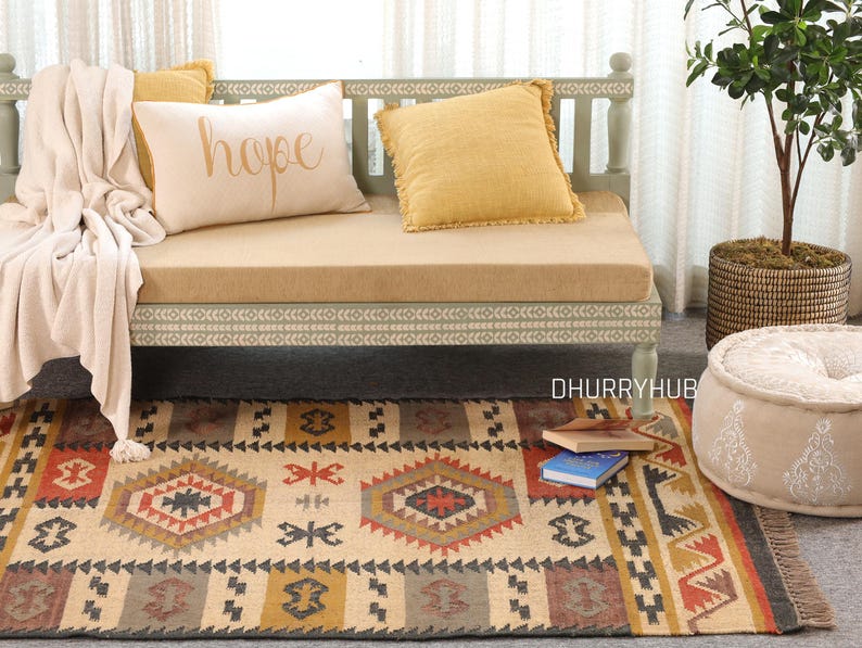 May include: A light green wooden daybed with a beige cushion and throw blanket. The daybed has a white and gray patterned trim. The daybed is decorated with three throw pillows, one with the word "hope" embroidered on it. A beige and brown patterned rug is in front of the daybed.