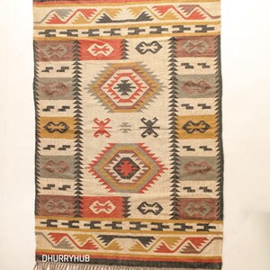 May include: A handwoven rug with a geometric pattern in shades of red, orange, yellow, black, and gray. The rug has a fringe border and is made of natural fibers.