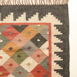 May include: A colourful rug with a geometric pattern of diamonds in shades of red, orange, green, blue, and white. The rug has a black border with a white fringe.