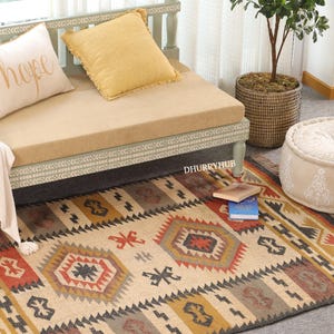 May include: A light green wooden bench with a beige cushion and two throw pillows. The bench is sitting on a beige and black patterned rug with red, yellow, and orange accents. The rug has a geometric design.