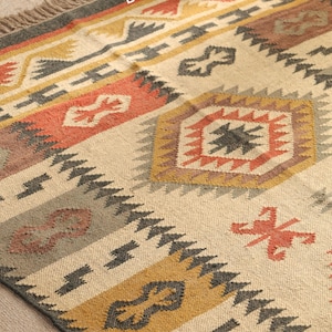 May include: A beige, gray, orange, and yellow patterned rug with a geometric design. The rug has a fringe border.