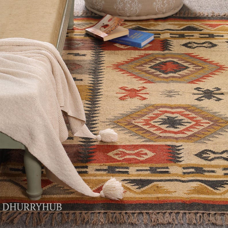 May include: A beige and brown rug with a geometric pattern and tassels. The rug has a red, black, and yellow design. The rug is on a wooden floor.