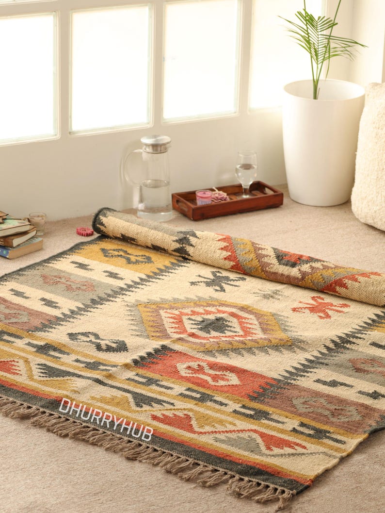 May include: A handwoven rug with a geometric pattern in shades of beige, brown, red, and yellow. The rug has fringe on all sides and the text "DHURRYHUB" is visible in the lower left corner.