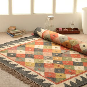 May include: A colourful, geometric patterned rug with a black border and fringe. The rug is made of wool and has a hand-woven look.