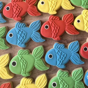 May include: A collection of colorful fish-shaped cookies. The cookies are decorated with red, yellow, blue, and green icing, featuring detailed fins and a black eye. These treats are perfect for a themed party or a sweet gift.