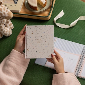 May include: A white and beige speckled notebook with the text "All my favourite people" in gold lettering. The notebook is open to a monthly calendar page.