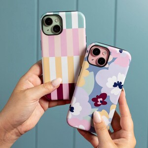 May include: Two phone cases with vibrant designs. One case has vertical stripes in pastel shades, including pink, yellow, and burgundy. The other case features a floral pattern with blue, pink, and yellow flowers. Both cases have a glossy finish.