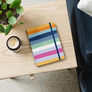 May include: A colourful striped notebook with a blue elastic closure. The notebook has the text "To Do Or Not To Do" printed on the cover.