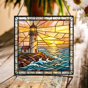May include: A square stained glass panel featuring a lighthouse on a rocky shore at sunset. The scene depicts a white lighthouse with a glowing lantern room, a dark sea with white-capped waves, and a sky filled with orange and yellow glass segments.