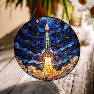 May include: A stained glass window hanging with a chain, depicting a rocket ship launching into a starry night sky. The rocket is white with red and blue accents, and the flames are orange and yellow.
