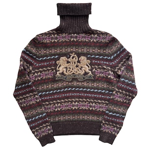 Puede incluir: Un jersey de cuello alto marrón con un diseño estampado en tonos burdeos, verde y morado. El jersey presenta un escudo con dos leones dorados y el texto "Ralph Lauren".