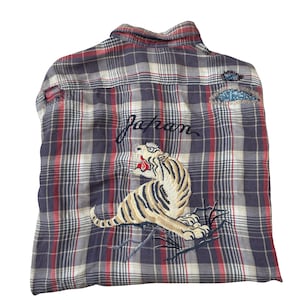 Op de afbeelding: Geruit overhemd in blauw, rood en wit. De achterkant van het overhemd heeft een geborduurde tijger en het woord "Japan". Het overhemd heeft een klassieke kraag en manchetten met knopen.