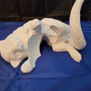 May include: White ceramic sculpture of a cat curled up in a sleeping position. The sculpture is detailed with realistic features, including a curled tail and paws.