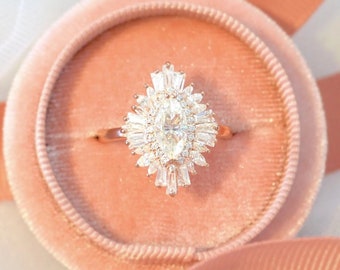 Könnte beinhalten: Ein Verlobungsring aus Roségold mit einem großen ovalen Mittelstück, das von kleineren Baguette-förmigen Diamanten umgeben ist. Der Ring befindet sich in einer rosafarbenen Samt-Ringbox.
