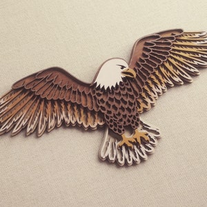 Pu&ograve; includere: Un'aquila di legno marrone e bianca con le ali spiegate. L'aquila &egrave; finemente intagliata con piume a strati e una testa dettagliata.