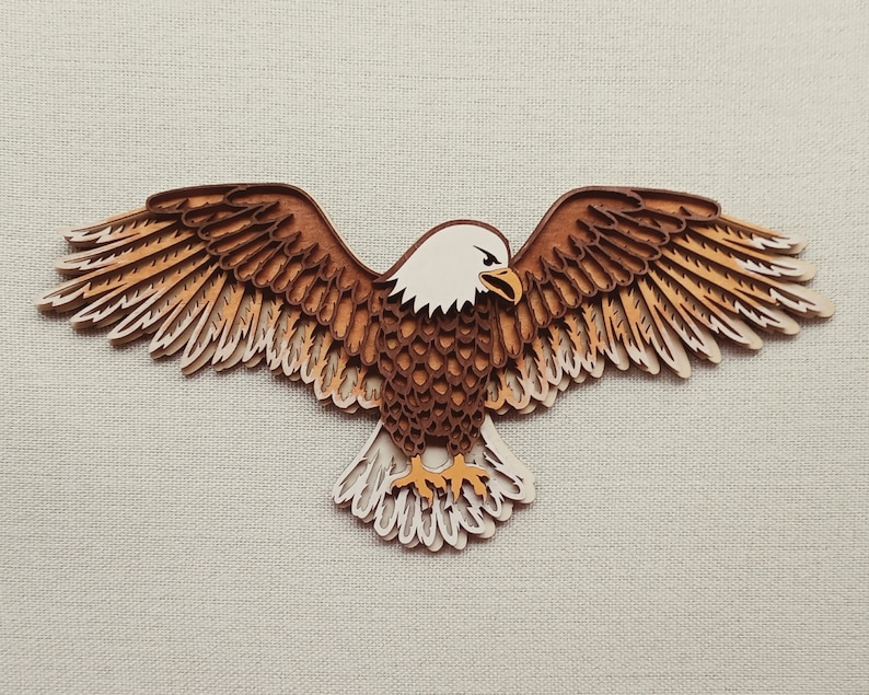 Pu&ograve; includere: Un ritaglio di legno di un'aquila calva con piume marroni e bianche. L'aquila &egrave; in volo con le ali spiegate. La testa dell'aquila &egrave; girata di lato e il suo becco &egrave; aperto.
