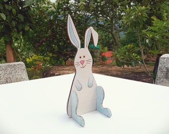 May include: A white rabbit cutout with blue ears and feet. The rabbit is sitting on a white surface.