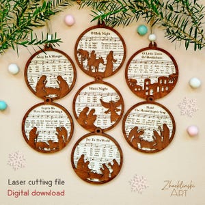 K&ouml;nnte beinhalten: Sieben runde Weihnachtsschmuckst&uuml;cke aus Holz mit lasergeschnittenen Krippenszenen und Liedtexten. Jedes Ornament hat eine dunkelbraune Oberfl&auml;che und ein Loch zum Aufh&auml;ngen. Die Lieder umfassen "Stille Nacht" und "Joy to the World".