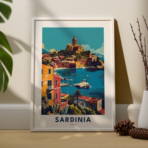May include: A framed poster with a colorful illustration of a coastal town in Sardinia, Italy. The poster features a blue sky, a turquoise sea, and a town with colorful buildings and a church on a hill. The text "SARDINIA ITALY" is printed at the bottom of the poster.