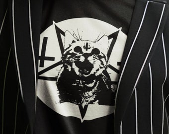 May include: A black and white striped blazer over a black t-shirt with a cat graphic inside a pentagram. The person in the image has green hair and is looking directly at the camera.