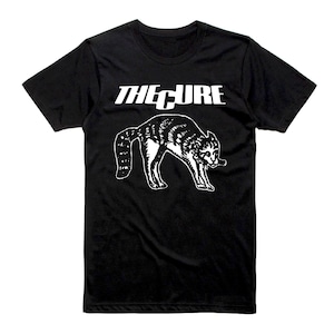 Op de afbeelding: Zwart t-shirt met de bandnaam "THE CURE" in witte blokletters boven een witte illustratie van een vosachtig wezen. Het t-shirt is gemaakt van een zacht materiaal en heeft korte mouwen.
