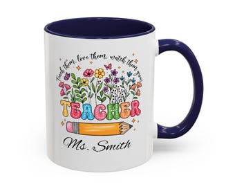 May include: White ceramic mug with a navy blue interior and handle. The mug features a colorful floral design with the word "TEACHER" in rainbow colors, a pencil, and the text "Teach them, love them, watch them grow." The name "Ms. Smith" is also printed on the mug.