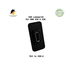 Könnte beinhalten: Schwarzes USB-Ladegerät für BMW E28 & E30 Modelle. Das Ladegerät verfügt über einen einzelnen USB-A-Anschluss und ist für den Einbau im Fahrzeug konzipiert. Der Text auf dem Ladegerät lautet "USB Ladegerät für BMW E28 & E30" und "Mit 1x USB-A".