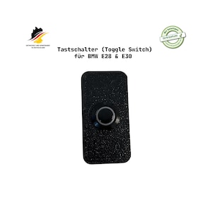 Könnte beinhalten: Schwarzer Kippschalter für BMW E28 & E30 Modelle. Der Schalter hat eine strukturierte Oberfläche und einen kreisförmigen Knopf mit einem silbernen Ring. Der Text "Tastschalter (Toggle Switch) für BMW E28 & E30" ist sichtbar.