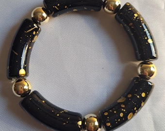 May include: Black and gold bracelet with round beads. The beads are black with gold speckles. The bracelet is made of glass and metal.
