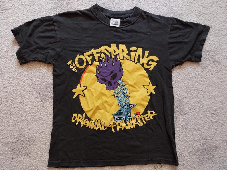 May include: Black t-shirt featuring a graphic of a purple skull with flames, a yellow circle, and the text "The Offspring Original Prankster." Two yellow stars flank the circle. The shirt is short-sleeved.