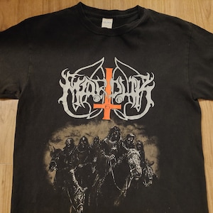 Puede incluir: Camiseta negra con un gráfico blanco y gris de la banda "Watain" con una cruz invertida roja. El gráfico también incluye un grupo de figuras a caballo.