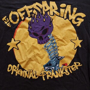 May include: Black t-shirt featuring a graphic of a purple skull with flames, a jack-in-the-box, and the text "OFFSPRING ORIGINAL PRANKSTER" in yellow. Two yellow stars are on either side of the design.