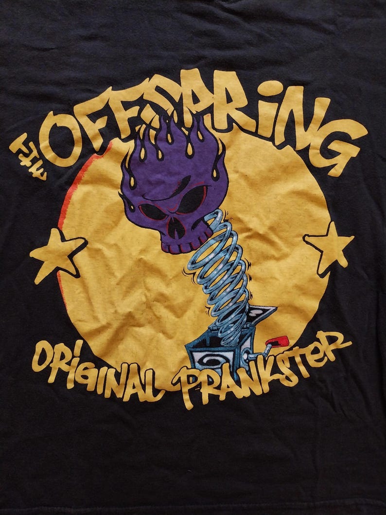 May include: Black t-shirt featuring a graphic of a purple skull with flames, a jack-in-the-box, and the text "OFFSPRING ORIGINAL PRANKSTER" in yellow. Two yellow stars are on either side of the design.