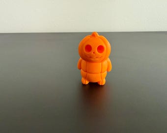 May include: A small, orange, Halloween-themed figurine shaped like a pumpkin with a smiling face and arms. The figurine has a carved-out face with round eye holes and a smiling mouth. The body is segmented with vertical lines.
