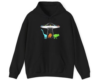 以下が含まれることがあります： 3匹の恐竜の上にホバリングしているUFOのグラフィックが描かれた黒いパーカー。恐竜は青、オレンジ、緑です。