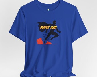 以下が含まれることがあります： ロイヤルブルーのTシャツに、スーパーヒーローが飛んでいるグラフィックと「SUPER DAD」という黄色の文字がプリントされています。