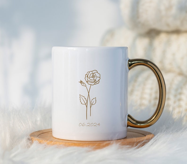 May include: White ceramic mug with a gold handle. The mug has a gold outline of a rose and the date 06.2024 printed on the front.