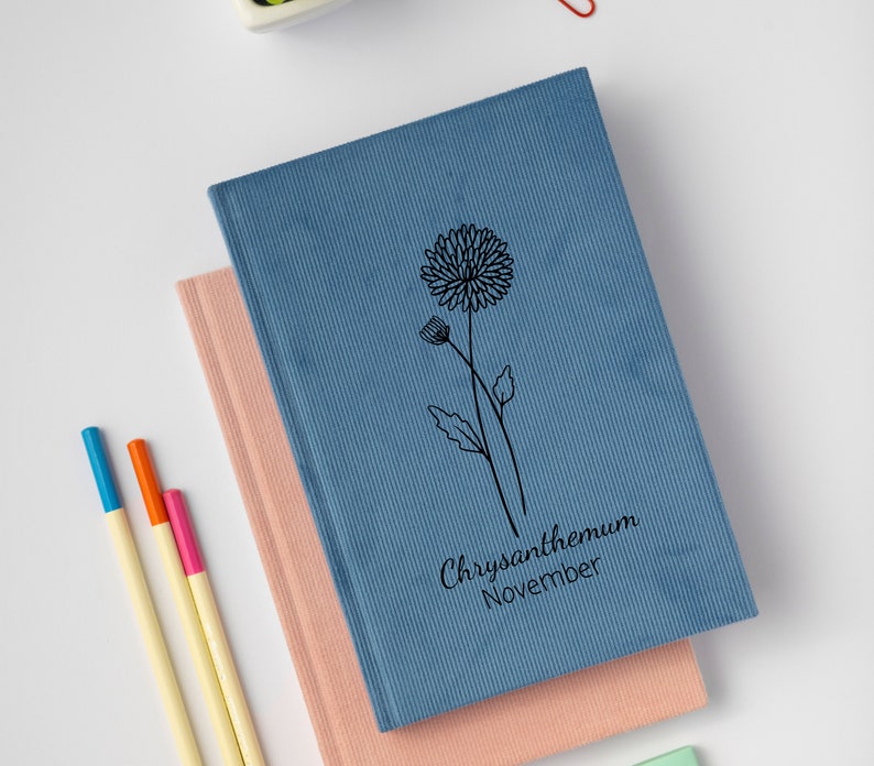 May include: Two notebooks stacked on top of each other. The top notebook is blue with a black line drawing of a chrysanthemum flower and the text "Chrysanthemum November". The bottom notebook is pink.