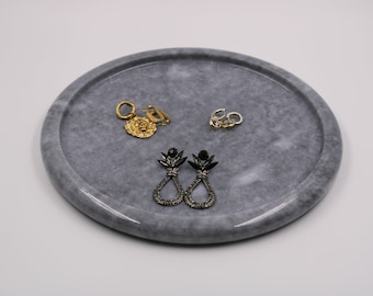 May include: A gray marble tray with a raised edge, featuring three pairs of earrings. Two pairs are gold and one pair is black with rhinestones.