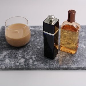 Könnte beinhalten: Ein graues Marmortablett mit einer Kerze aus Glas, einer blauen Glasflasche mit Parfüm und einer braunen Glasflasche mit Kölnisch Wasser.