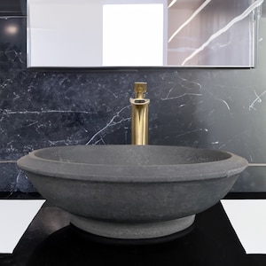 May include: A dark grey stone sink with a gold tap. The sink is on a black countertop with a white tile border.