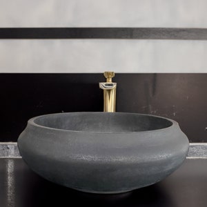 May include: A dark gray, round, ceramic sink with a gold faucet. The sink is set against a black and white tiled background.