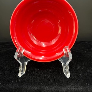 May include: A bright red ceramic bowl with a smooth, glossy finish. The bowl is empty and is sitting on a clear plastic stand.