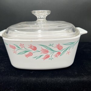 May include: White casserole dish with a clear glass lid. The dish is decorated with a floral pattern of pink tulips and green leaves. The dish has two handles and a clear glass knob on the lid.