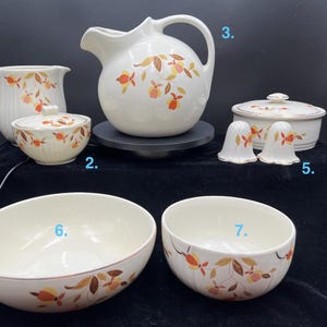 May include: A collection of vintage white ceramic serving dishes with a leaf pattern in orange, yellow, and brown. Includes a pitcher, sugar bowl, covered dish, salt and pepper shakers, and two bowls. The pitcher is approximately 9 inches tall.