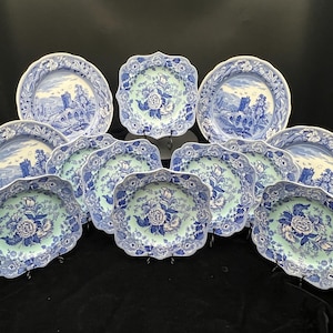 May include: A collection of blue and white ceramic plates and serving dishes. The plates feature a landscape scene with a castle and bridge. The serving dishes have a floral design. The edges of the plates and dishes are scalloped.