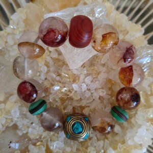 May include: A bracelet made of clear quartz, red agate, and turquoise beads. The bracelet has a gold metal charm with a turquoise inlay.