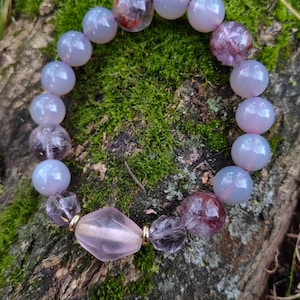 May include: A bracelet made of purple and clear beads with a pink and gold bead in the center.